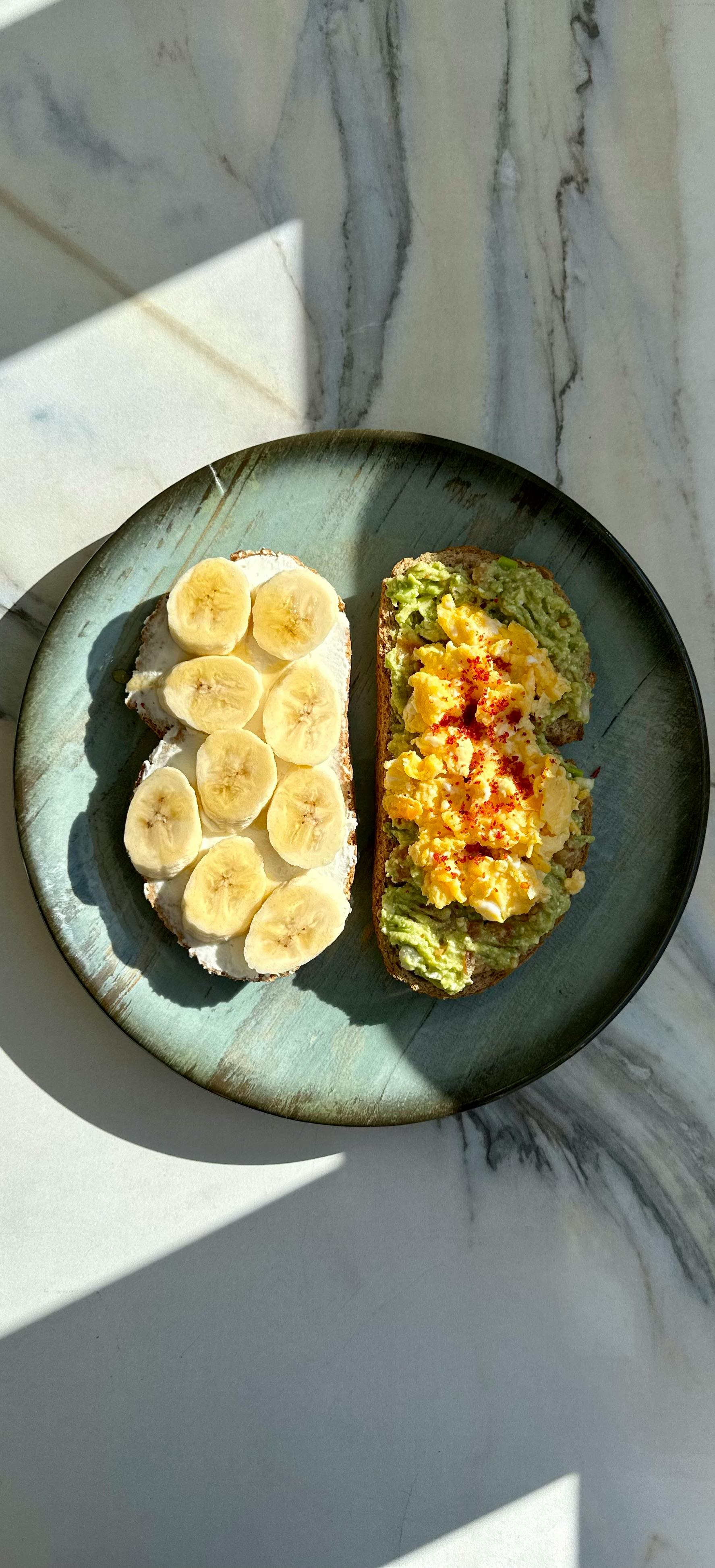 Two slices of avocado toast — one with scrambled egg and one with banana and cream